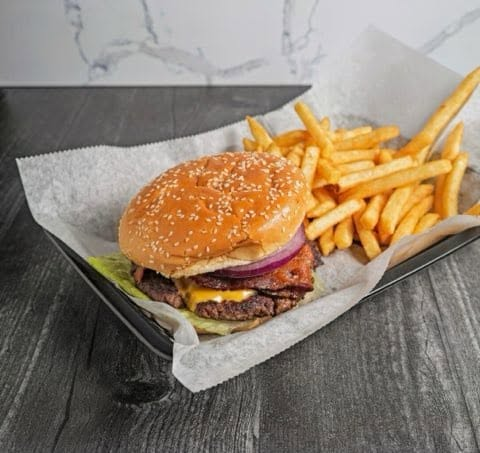 Classic burger with bacon, cheese and red onion in a basket with seasoned fries
